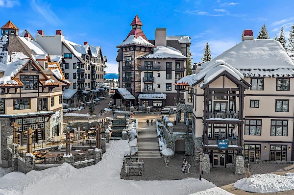 A picturesque winter village with snow-covered buildings, adorned in a charming architectural style, surrounded by a bright blue sky and trees.