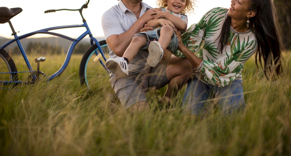 A family is enjoying time together in a grassy field with a bicycle in the background, all appearing happy and playful.