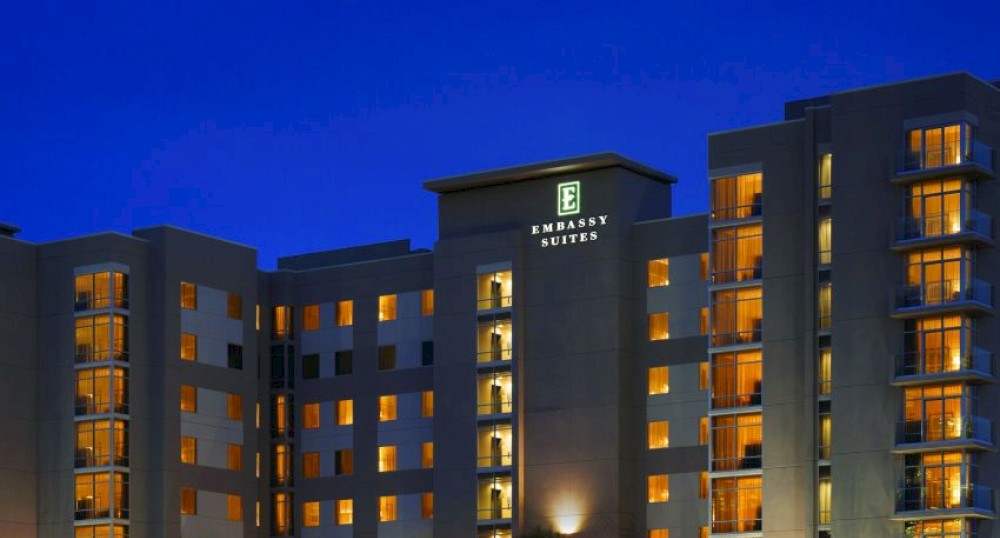 The image shows a well-lit multi-story hotel building at night, reflecting off a nearby body of water, with a sign displaying "Embassy Suites."