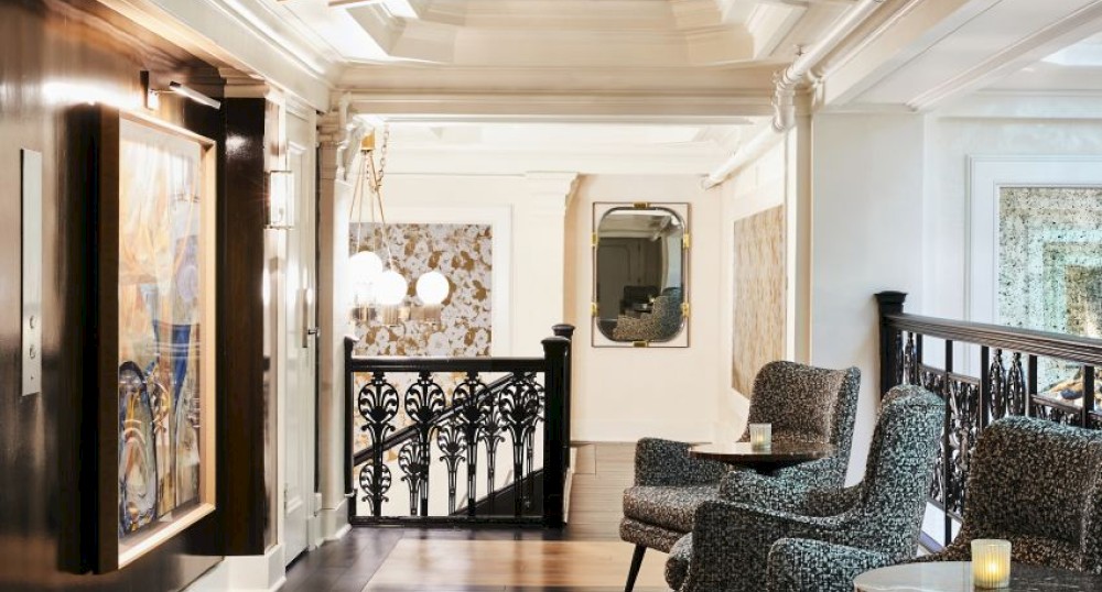 A stylishly furnished lounge area with patterned chairs, wooden flooring, elegant lighting, and art hanging on the walls under a coffered ceiling.