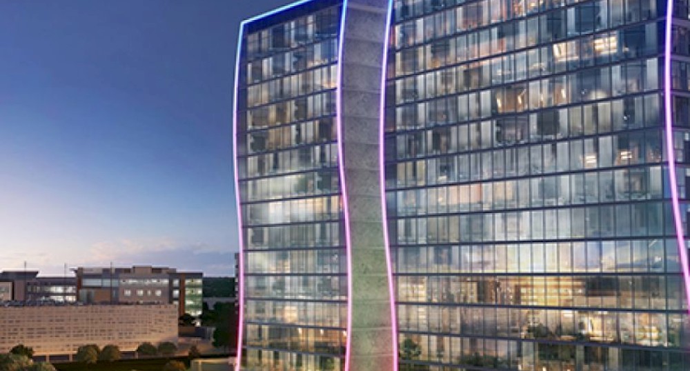 The image depicts a modern, glass-fronted building with the word "WAVE" on top. It has a unique, wavy design and is lit up at night.