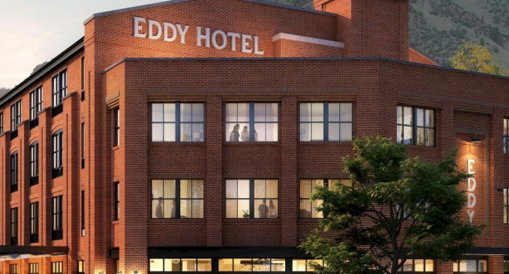 This image shows a red-brick building labeled "Eddy Hotel" with cars and people outside, set against a backdrop of hills and trees.