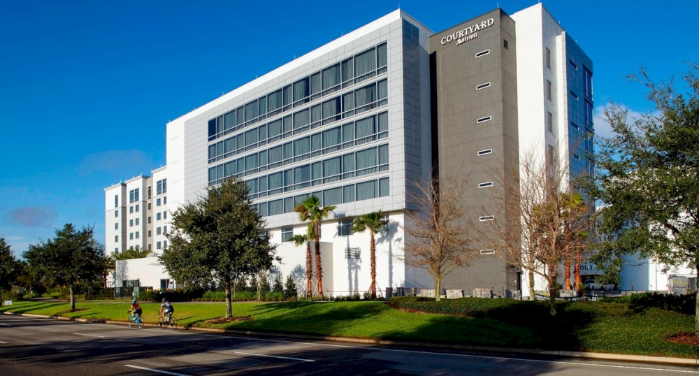 The image shows a modern, multi-story building with "Courtyard" signage, surrounded by trees and a wide road in the foreground.