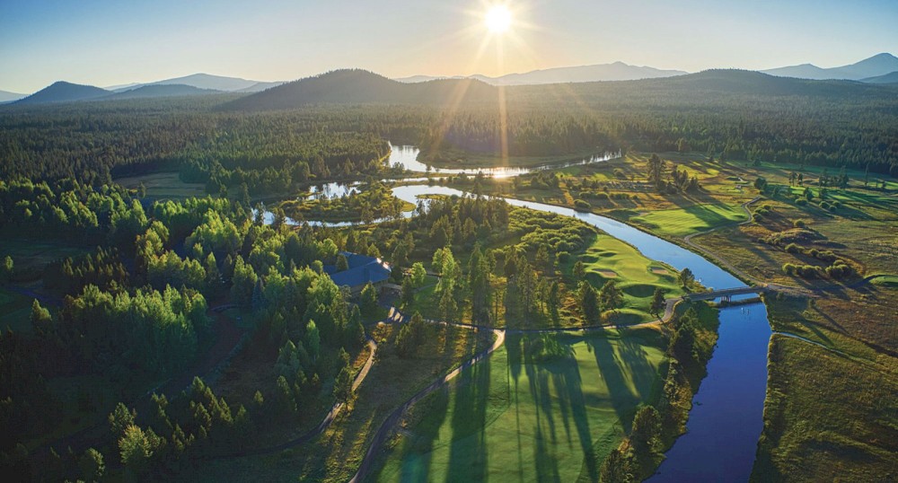 A picturesque landscape of a river winding through a forested area with the sun setting over distant mountains.
