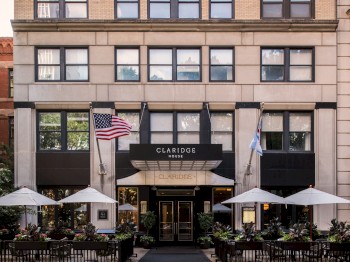 The image shows the front entrance of Claridge House, featuring flags, outdoor seating with umbrellas, and a welcoming pathway leading inside.