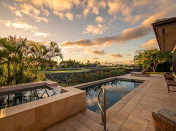 A luxurious poolside scene with a view of palm trees and a beautiful sunset sky, adjacent to a modern building.